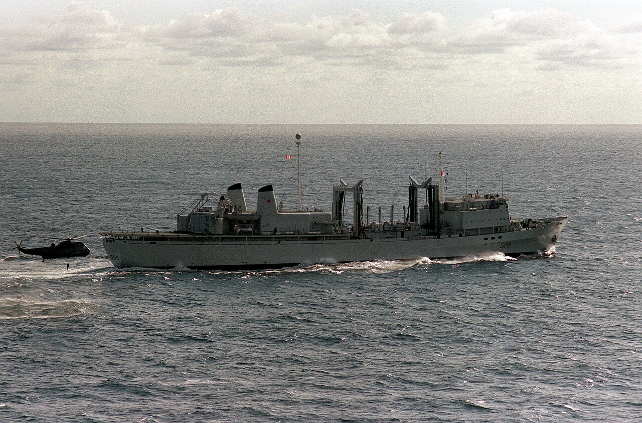 An aerial starboard beam view of the Canadian replenishment ship HMCS PROTECTEUR (AOR-509) underway during NATO exercise Northern Wedding '86. A British Royal Navy Sea King helicopt - DPLA - 484e36502d9eb0a27c13f641b36d5d62.jpeg